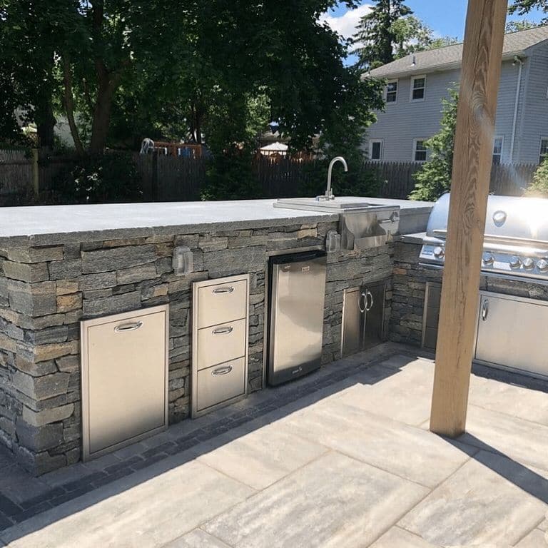 Application image for Black Ash Granite. The image shows this material being used for full bed veneer and thin veneer. The surface finish shown is split-face. Dominant colors shown are gray and tan; with blue, orange/rust and purple secondaries. The color mix creates a cool feeling.