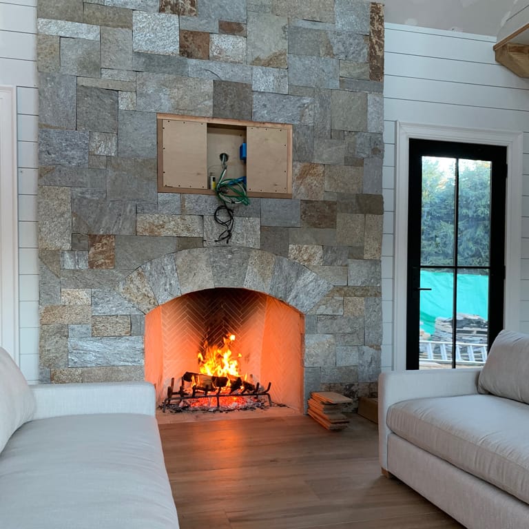 Feature image for Granite - Spruce Mountain. The image shows this material being used for fireplace surround, thin veneer and interior cladding. Dominant colors shown are beige, blue and gray; with brown and green secondaries. Exhibits "movement" and the color mix creates a warm feeling. Streaked, speckled, blotched, random and coarse speckled color patterns.