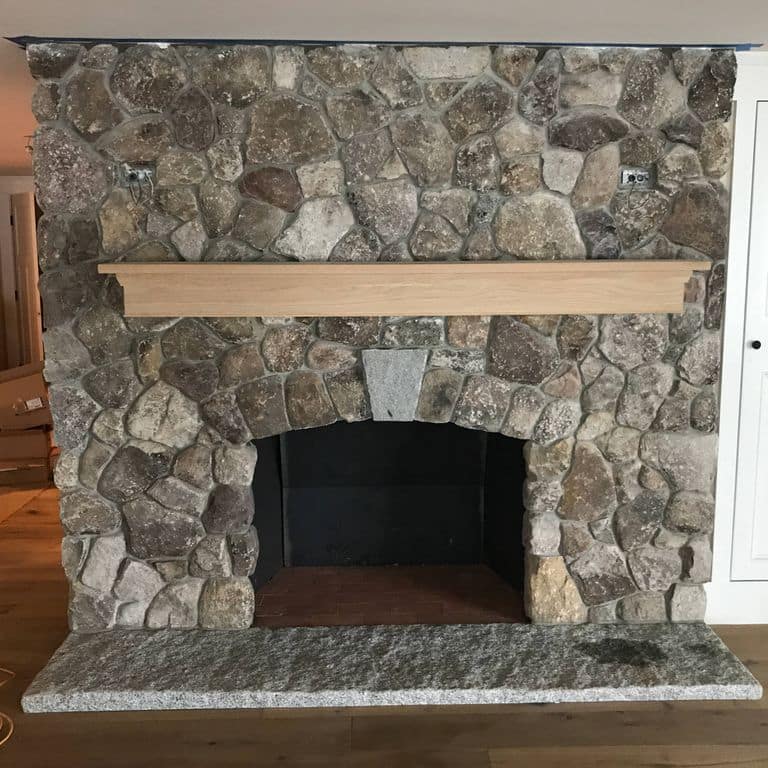 Application image for Fieldstone - Old New England Round. The image shows this material being used for fireplace hearth, thin veneer and interior cladding. Dominant colors shown are brown and gray. The color mix creates a warm feeling.
