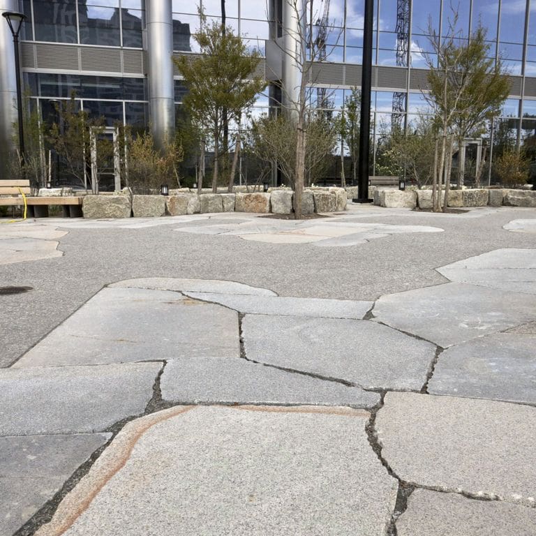 Application image for Granite - New England Mix. The image shows this material being used for patio pavers and public area. The dominant color shown is gray. The color mix creates a warm feeling.