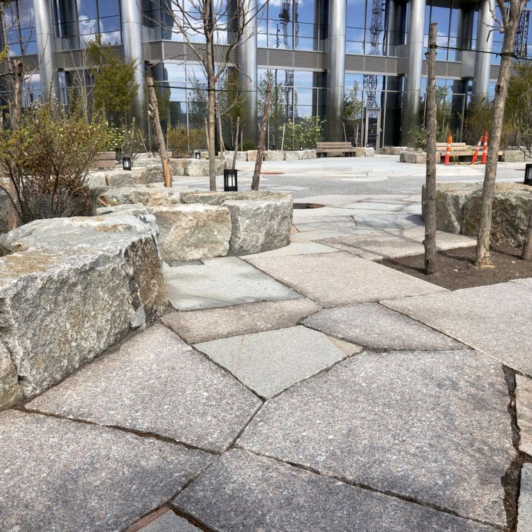 Application image for Granite - New England Mix. The image shows this material being used for patio pavers and public area. The dominant color shown is gray.