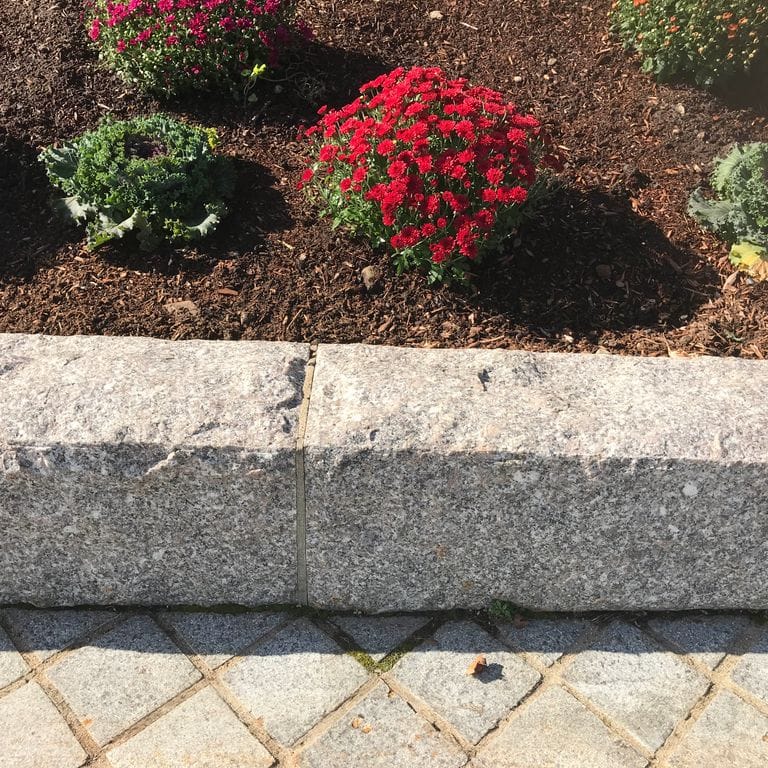 Application image for Deer Isle Granite. The image shows this material being used in a landscape curbing &amp; edging application. The dominant color shown is gray.