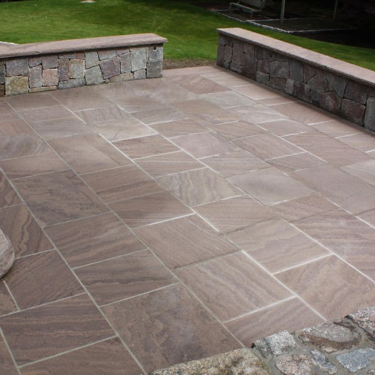 Feature image for Brown Wave Sandstone. The image shows this material being used for wallstone cap, patio pavers and monolithic steps. Dominant colors shown are brown, gray and purple. The color mix creates a warm feeling. Swirled, streaked and cloudy color patterns.