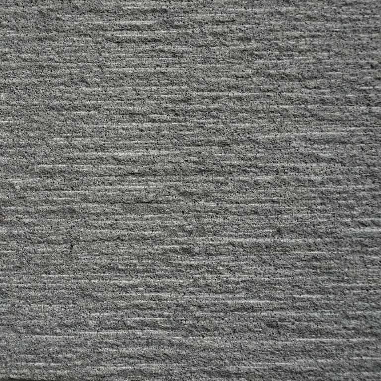 Color/Finish variation image for Ankar Gray Basalt. The surface finishes shown are coarse adze and brushed. The dominant color shown is gray; with brown and green secondaries. The color mix creates a cool feeling. Fine speckled and linear color patterns.