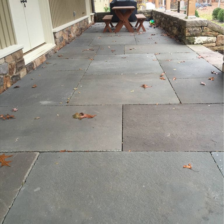 Feature image for Bluestone Natural Cleft - Blue/Gray. The image shows this material being used in a patio pavers application. The dominant color shown is gray. The color mix creates a cool feeling. Solid, regular and cloudy color patterns.