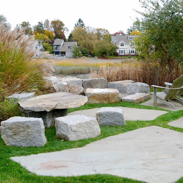 Application image for Bluestone Natural Cleft - Green/Brown. The image shows this material being used in a patio pavers application. The surface finish shown is natural cleft. Dominant colors shown are beige and gray. The color mix creates a cool feeling.