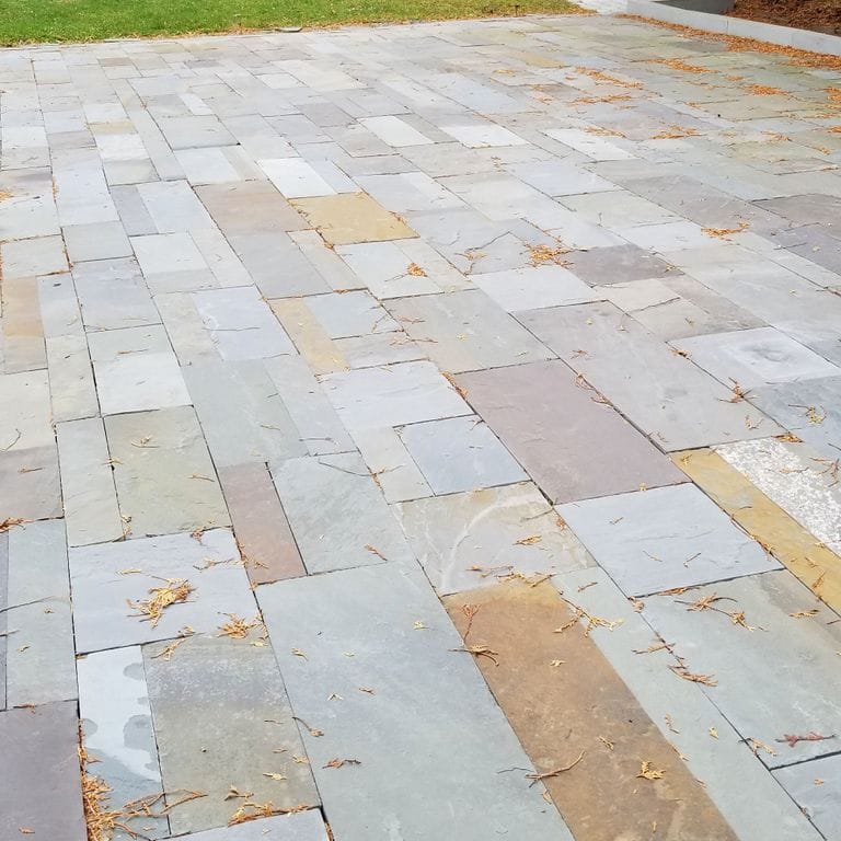 Application image for Full Color Mix Bluestone - Natural Cleft. The image shows this material being used in a patio pavers application. Dominant colors shown are blue, gray and orange/rust.