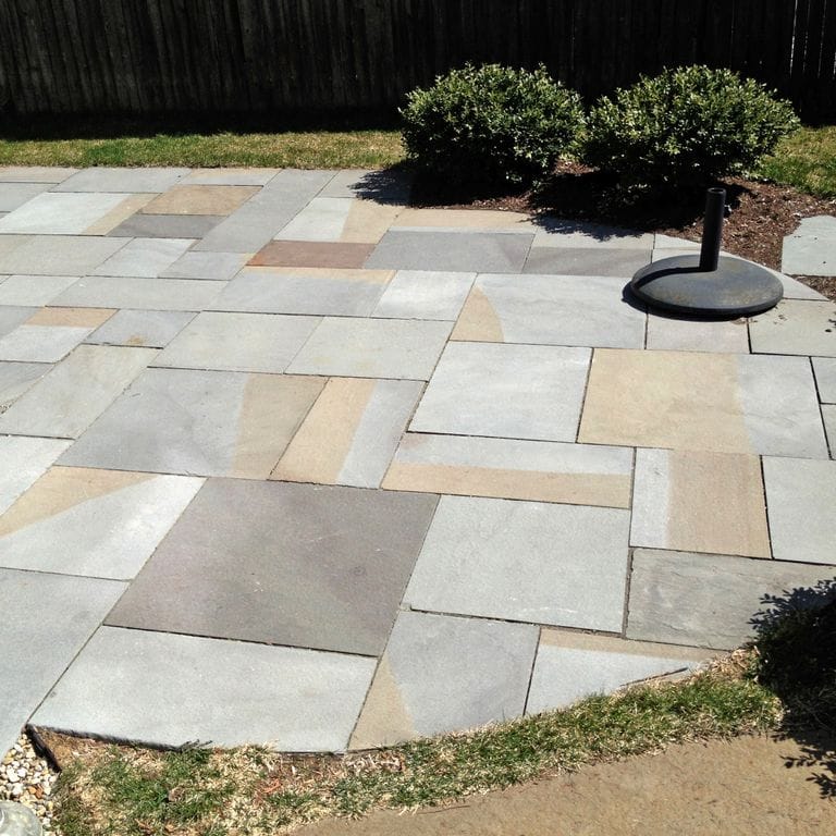 Feature image for Bluestone Flamed Surface - Full Color. The image shows this material being used in a patio pavers application. The dominant color shown is gray; with beige, brown, orange/rust, pink, white, tan and cream secondaries. The color mix creates a warm feeling. Random color pattern.
