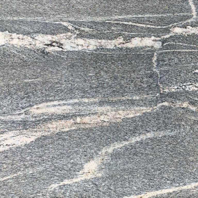 Close-up image for Black Mountain Granite - Worked Surface. The surface finish shown is flamed. The dominant color shown is gray; with beige, pink, white and cream secondaries. Exhibits "movement" and the color mix creates a cool feeling. Fine speckled, veined and streaked color patterns.