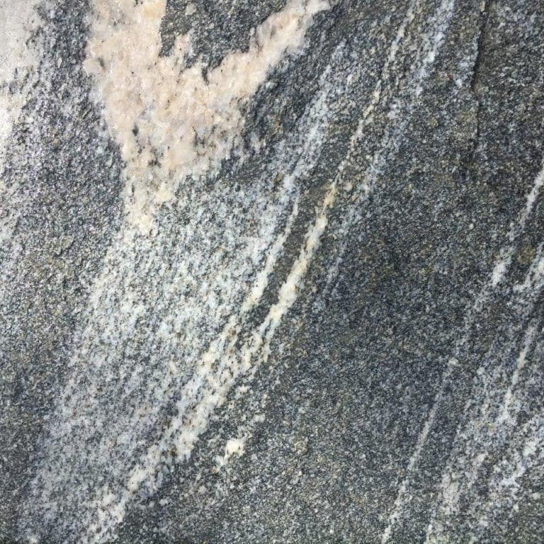 Feature image for Black Mountain Granite - Worked Surface. The dominant color shown is gray; with beige, black, blue, brown, green, purple, white and cream secondaries. The color mix creates a cool feeling. Random, fine speckled, blotched and streaked color patterns.