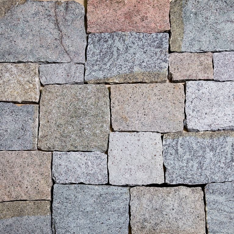 Best close-up image for Adirondack Elite Granite. The image shows this material being used for patio pavers, full bed veneer and thin veneer. The surface finish shown is split-face with flat plane. The dominant color shown is gray; with beige, blue, brown, orange/rust, pink, purple, white and tan secondaries. Exhibits "movement" and the color mix creates a warm feeling. Linear, speckled and random color patterns.