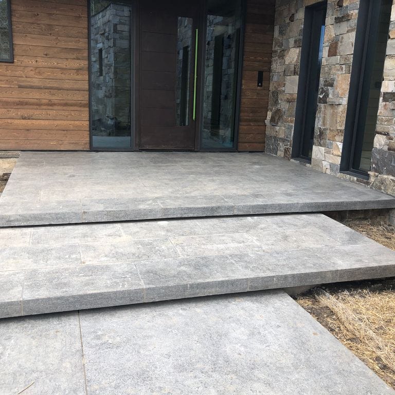 Application image for Highland Limestone. The image shows this material being used for path pavers, landings and monolithic steps. The surface finish shown is flamed. The dominant color shown is gray. The color mix creates a warm feeling. Regular and random color patterns.