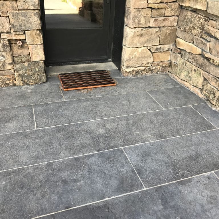 Application image for Highland Limestone. The image shows this material being used in a patio pavers application. The surface finish shown is flamed. The dominant color shown is gray. The color mix creates a warm feeling. Regular and random color patterns.