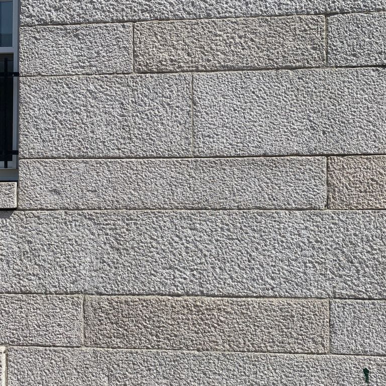 Application image for Chelmsford Gray Granite. The image shows this material being used in a full bed veneer application. The surface finish shown is coarse bush hammered. The dominant color shown is gray. The color mix creates a cool feeling. Speckled color pattern.