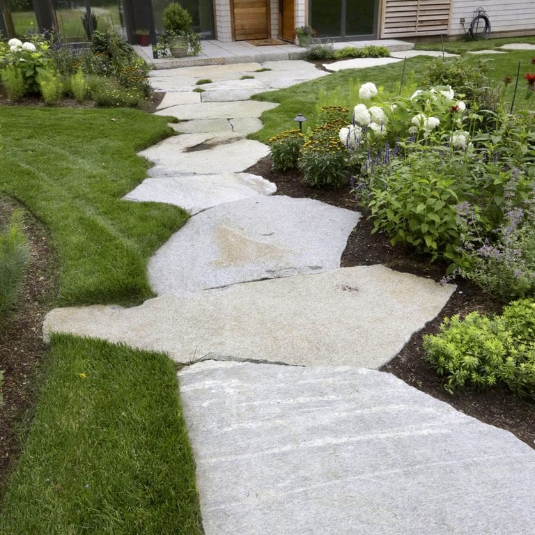 Application image for Dodlin Hill Granite. The image shows this material being used in a path pavers application. The surface finish shown is natural cleft. The dominant color shown is gray; with beige, brown and white secondaries. Exhibits "movement" and the color mix creates a warm feeling. Fine speckled and veined color patterns.
