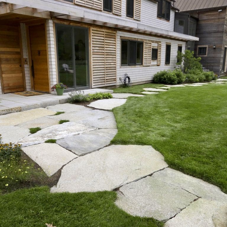 Application image for Dodlin Hill Granite. The image shows this material being used in a path pavers application. The surface finish shown is natural cleft. The dominant color shown is gray; with beige, brown, white, tan and cream secondaries. Exhibits "movement" and the color mix creates a warm feeling. Veined and speckled color patterns.