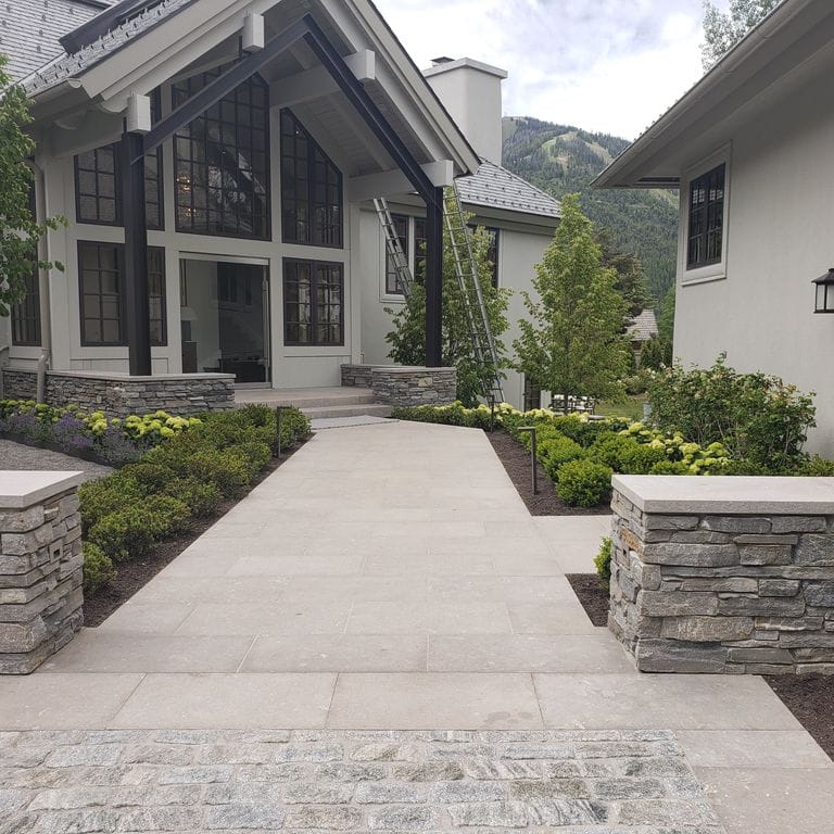 Application image for Limestone - Portuguese Dawn Haze. The image shows this material being used for wallstone cap and path pavers. The dominant color shown is gray.