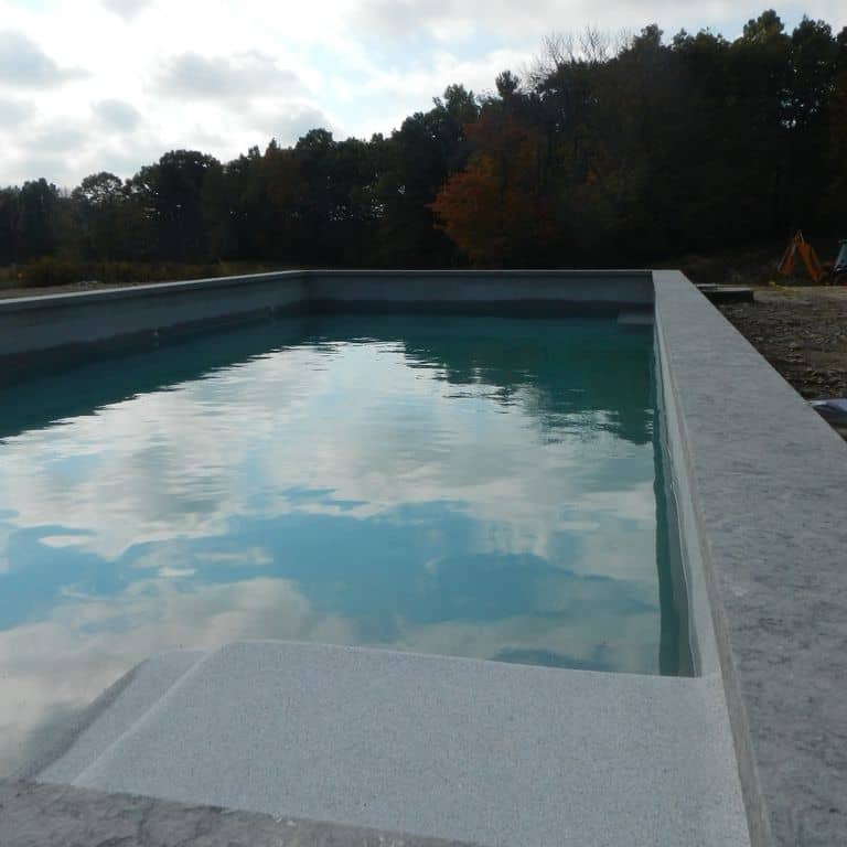 The image shows this material being used for pool coping, pool deck pavers and . The surface finish shown is flamed. The dominant color shown is gray; with a purple secondary. The color mix creates a cool feeling. Regular color pattern.