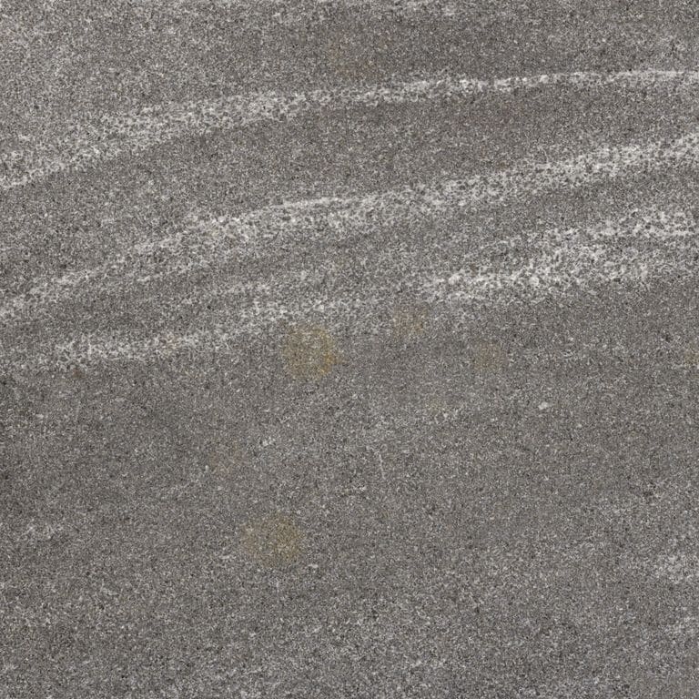 Close-up image for Jet Mist Granite. The surface finish shown is flamed. The dominant color shown is gray; with brown, green, purple, white and tan secondaries. Exhibits "movement". Fine speckled and streaked color patterns.