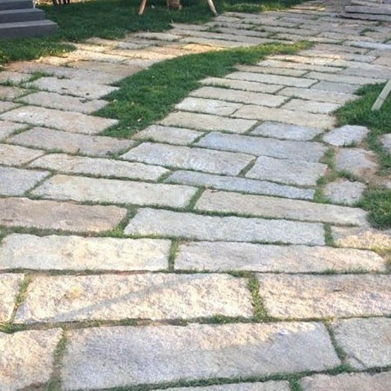 Application image for Reclaimed Rustic Granite. The image shows this material being used in a driveway pavers application. The surface finish shown is . The dominant color shown is gray. The color mix creates a warm feeling.