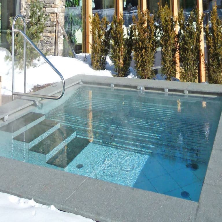Feature image for Porphyry Worked Surface - Gray Real. The image shows this material being used in a pool coping and pool deck pavers. The dominant color shown is gray. The color mix creates a cool feeling. Solid and fine speckled color patterns.