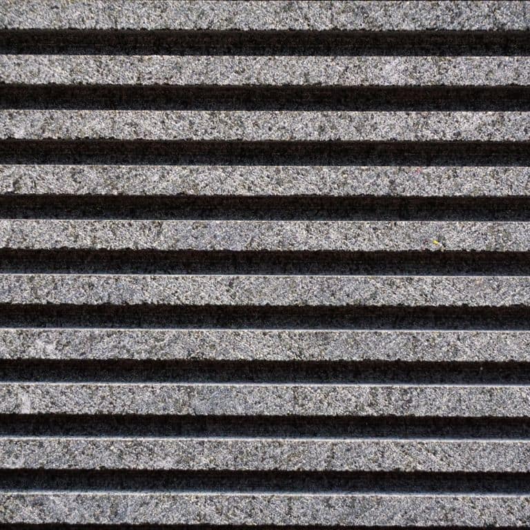 Color/Finish variation image for Ankar Black Basalt. The surface finish shown is grooved. Dominant colors shown are black and gray; with brown, purple and white secondaries. The color mix creates a cool feeling. Speckled and linear color patterns.