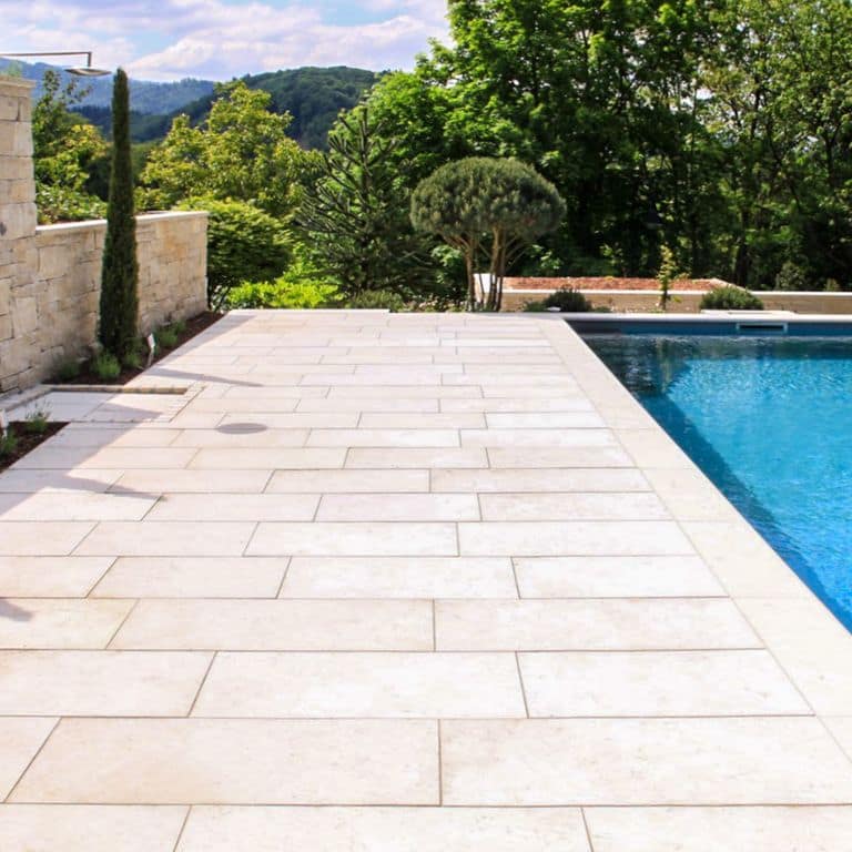 Application image for Bavarian Limestone - Beige. The image shows this material being used for pool coping and pool deck pavers. The dominant color shown is cream. The color mix creates a warm feeling. Regular and random color patterns.