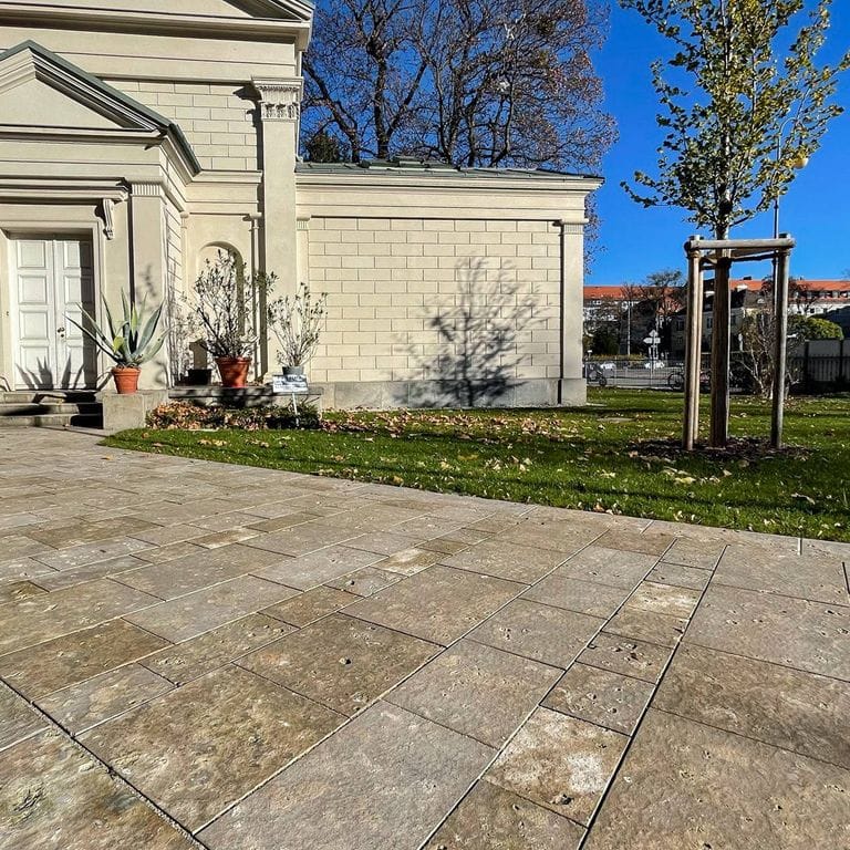 Application image for Bavarian Dolomite - Gray. The image shows this material being used for driveway pavers and patio pavers. The surface finish shown is flamed. Dominant colors shown are brown, gray and tan; with beige and orange/rust secondaries. The color mix creates a warm feeling. Random color pattern. Contains mineral inclusions.