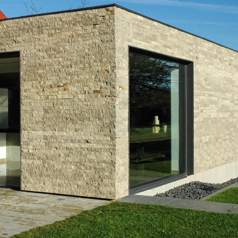 Application image for Bavarian Dolomite - Gray. The image shows this material being used for full bed veneer and thin veneer. The surface finish shown is split-face. Dominant colors shown are beige and tan. Blotched color pattern.