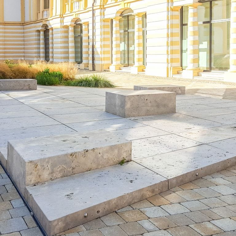 Application image for Bavarian Dolomite - Gray. The image shows this material being used for seating &amp; benches and patio pavers. The surface finish shown is flamed. Dominant colors shown are gray and tan. The color mix creates a warm feeling. Random color pattern. Contains voids.