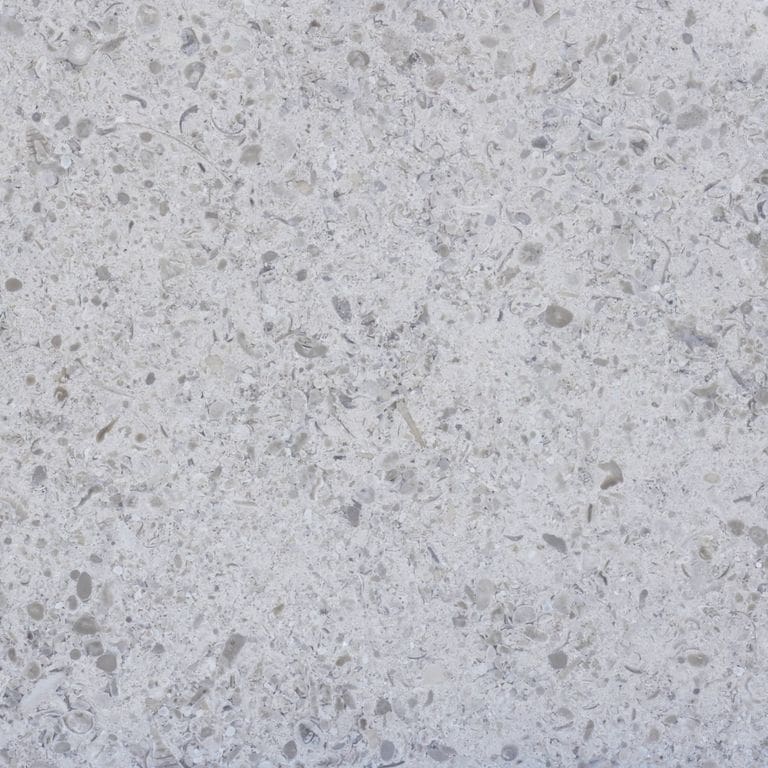 Close-up image for Ocean Blue Limestone. The surface finish shown is honed. Dominant colors shown are gray and white; with beige and blue secondaries. The color mix creates a cool feeling. Speckled and cloudy color patterns. Contains mineral inclusions.