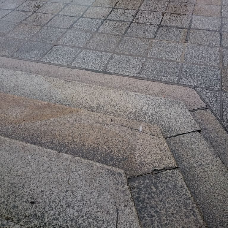 Close-up image for Reclaimed Granite Stair Blocks. The surface finishes shown are weathered and worn. The dominant color shown is gray; with brown, green and purple secondaries. The color mix creates a cool feeling. Speckled and coarse speckled color patterns.