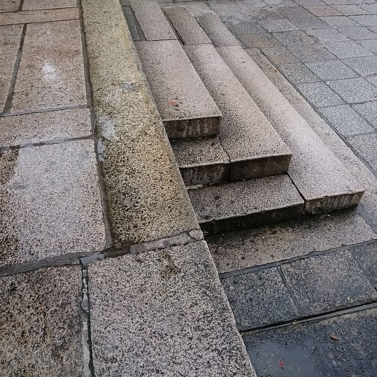 Application image for Reclaimed Granite Stair Blocks. The image shows this material being used in a monolithic steps application. The surface finish shown is a combination of weathered and worn. The dominant color shown is gray; with beige, black, blue, brown, green, purple, white and cream secondaries. The color mix creates a warm feeling. Speckled and blotched color patterns.