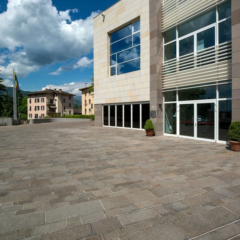 Feature image for Porphyry - Natural Surface - Gray Selected. The image shows this material being used for patio pavers and public area. The dominant color shown is gray; with blue, brown, green, purple and tan secondaries. Fine speckled and speckled color patterns.