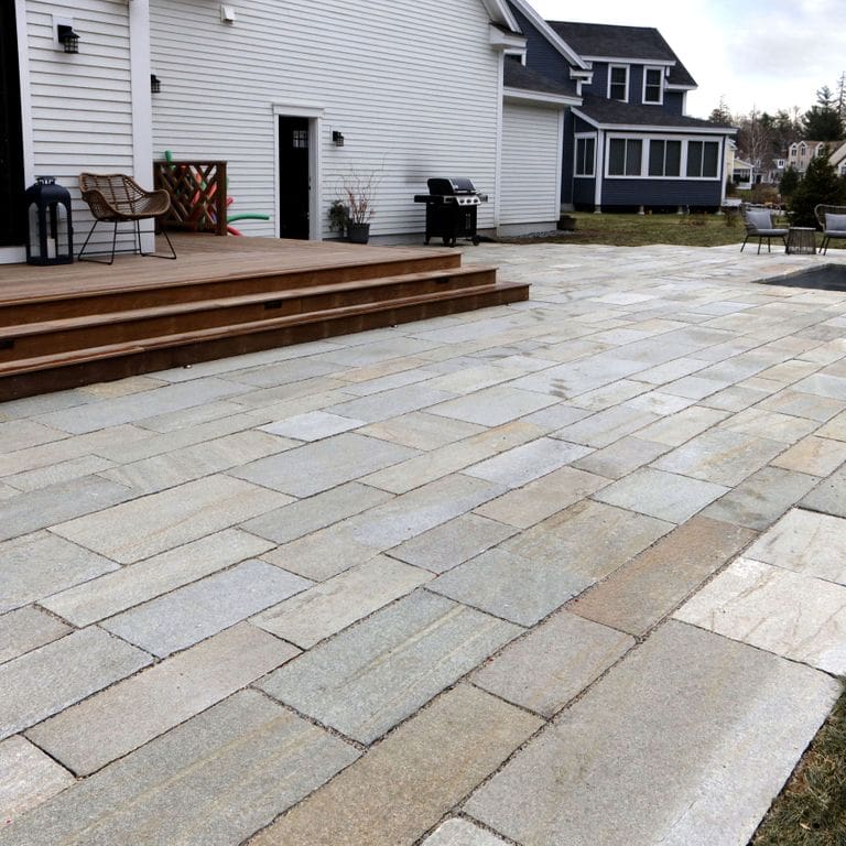 Application image for Pietra Italia Full Color Gneiss. The image shows this material being used for patio pavers and pool deck pavers. The surface finish shown is natural cleft. Dominant colors shown are beige and gray. Exhibits "movement" and the color mix creates a warm feeling. Regular, linear and cloudy color patterns. Contains some mica and mineral inclusions.