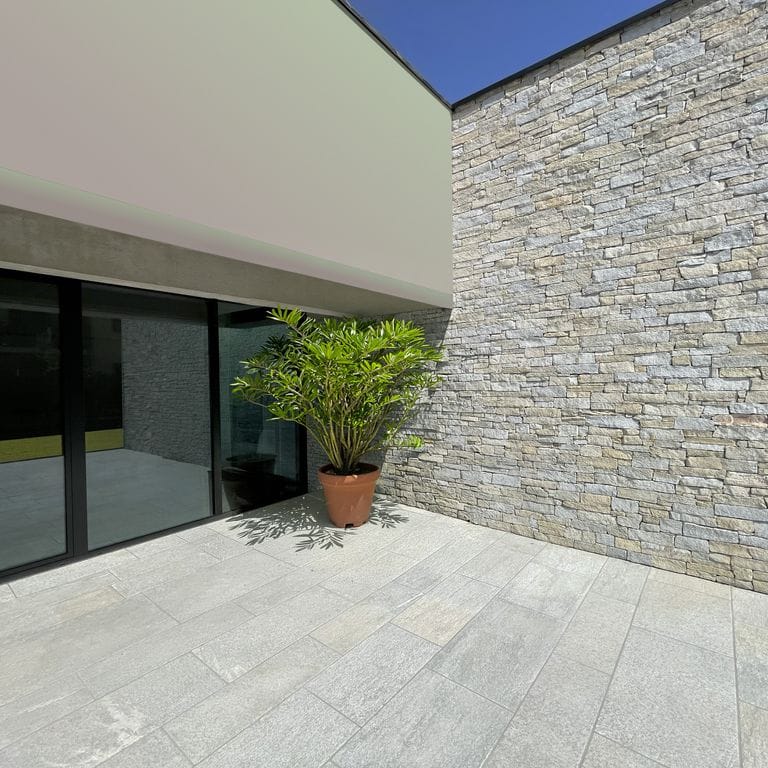 Application image for Pietra Italia Gneiss - Natural Cleft. The image shows this material being used for patio pavers and thin veneer. The surface finish shown is sand blasted. The dominant color shown is gray. The color mix creates a warm feeling.