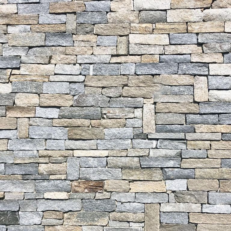 Application image for Pietra Italia Full Color Gneiss. The image shows this material being used for full bed veneer and thin veneer. The surface finish shown is split-face. Dominant colors shown are beige and gray; with beige, blue, brown, pink, white, tan and cream secondaries. The color mix creates a warm feeling. Regular and fine speckled color patterns.