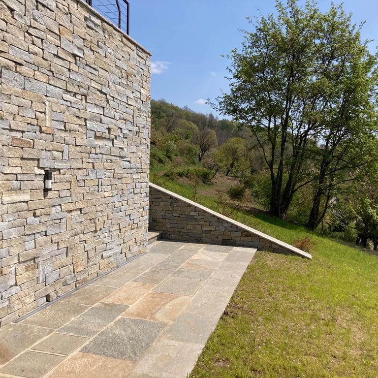 Application image for Pietra Italia Full Color Gneiss. The image shows this material being used for patio pavers, full bed veneer and thin veneer. The surface finish shown is natural cleft. Dominant colors shown are beige and tan; with brown, gray, orange/rust, pink and cream secondaries. The color mix creates a warm feeling.