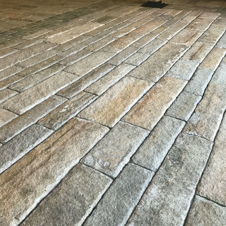 The image shows this material being used for interior floor and driveway pavers. The dominant color shown is gray; with beige, brown and orange/rust secondaries.