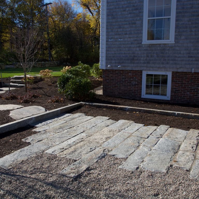 Application image for Granite - Reclaimed Second Generation Curbstone. The image shows this material being used in a driveway pavers application. The dominant color shown is gray; with blue and brown secondaries. Regular color pattern.