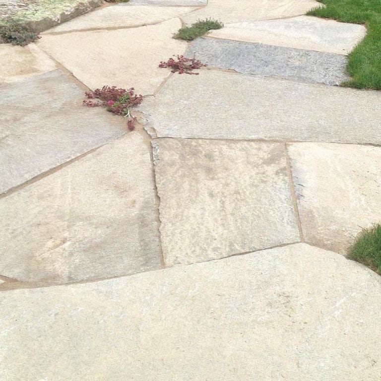 The image shows this material being used for path pavers and patio pavers. The surface finish shown is split-face. The dominant color shown is beige; with gray, white, tan and cream secondaries. Exhibits "movement" and the color mix creates a warm feeling. Regular, blotched and cloudy color patterns.