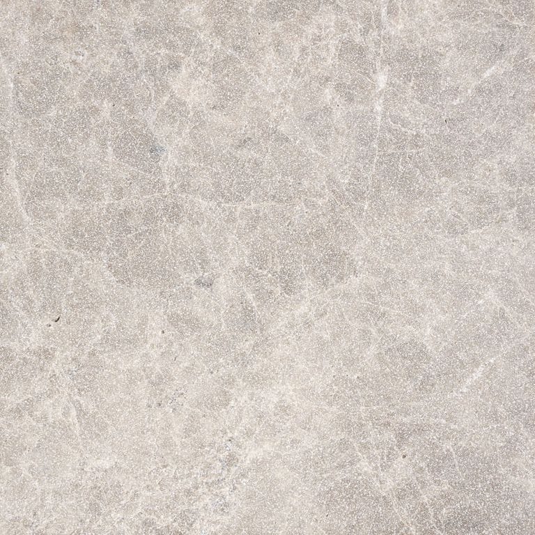 Swatch image for Dalmatian Limestone. The surface finish shown is a combination of brushed and sand blasted. Dominant colors shown are beige, gray and white; with pink, purple, tan and cream secondaries. The color mix creates a warm feeling. Veined and cloudy color patterns.