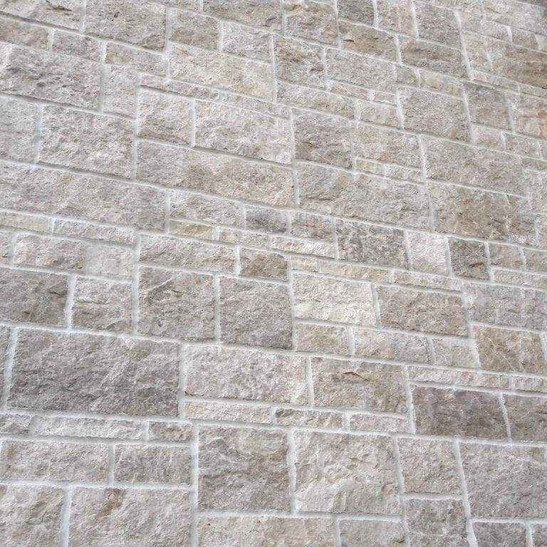 Application image for Dalmatian Limestone. The image shows this material being used for full bed veneer and thin veneer. The surface finish shown is split-face with flat plane. The dominant color shown is gray; with beige, blue, pink, purple, white and cream secondaries. The color mix creates a warm feeling. Cloudy color pattern.