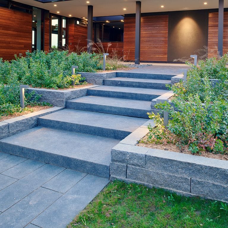 Application image for Superior Northern Granite. The image shows this material being used for landscape wallstone, path pavers and monolithic steps. The surface finish shown is flamed. Dominant colors shown are black and gray. The color mix creates a cool feeling.