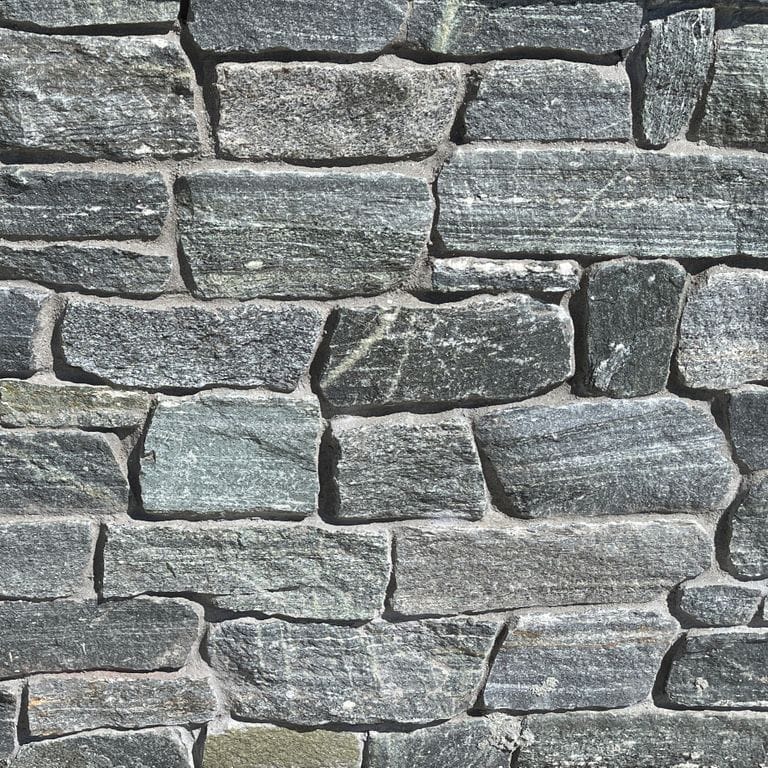 Best close-up image for Connecticut White Line Granite. The image shows this material being used in a landscape wallstone application. The surface finish shown is split-face. Dominant colors shown are gray and white; with blue, green and white secondaries. Exhibits "movement" and the color mix creates a cool feeling. Regular and linear color patterns.