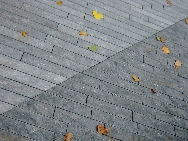 Application image for Kilkenny Limestone. The image shows this material being used in a patio pavers application. The surface finish shown is split-face with flat plane. Dominant colors shown are blue and gray. The color mix creates a cool feeling. Regular color pattern.