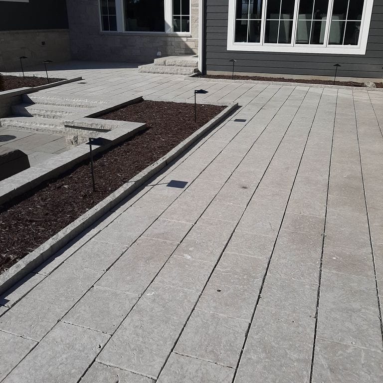 Application image for Madison Limestone. The image shows this material being used for wallstone cap, landscape curbing &amp; edging, patio pavers and monolithic steps. The surface finish shown is flamed. The dominant color shown is gray; with beige, blue, brown, purple and white secondaries. The color mix creates a cool feeling. Regular color pattern.