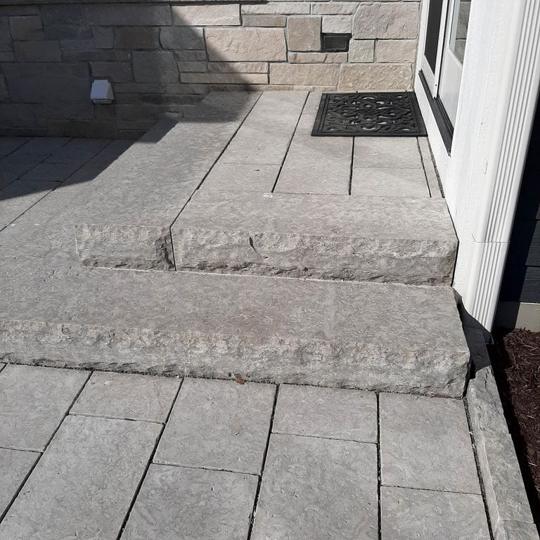 Application image for Madison Limestone. The image shows this material being used for landscape curbing &amp; edging, patio pavers and monolithic steps. The surface finish shown is flamed. The dominant color shown is gray; with beige, blue, purple and white secondaries. The color mix creates a cool feeling. Regular color pattern.