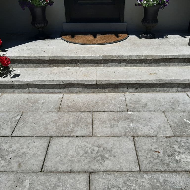 Application image for Madison Limestone. The image shows this material being used for path pavers, patio pavers and treads. The surface finish shown is flamed. The dominant color shown is gray; with beige and white secondaries. Regular color pattern.