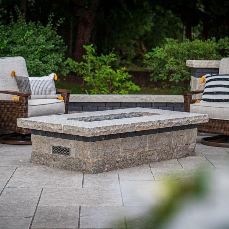 Application image for Madison Limestone. The image shows this material being used for outdoor fire concepts and patio pavers. The surface finish shown is flamed. The dominant color shown is gray; with beige and white secondaries. Regular color pattern.